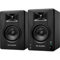 M-Audio BX3 BT desktop speakers shown on a desk with black and silver design, featuring control knobs and connection ports.