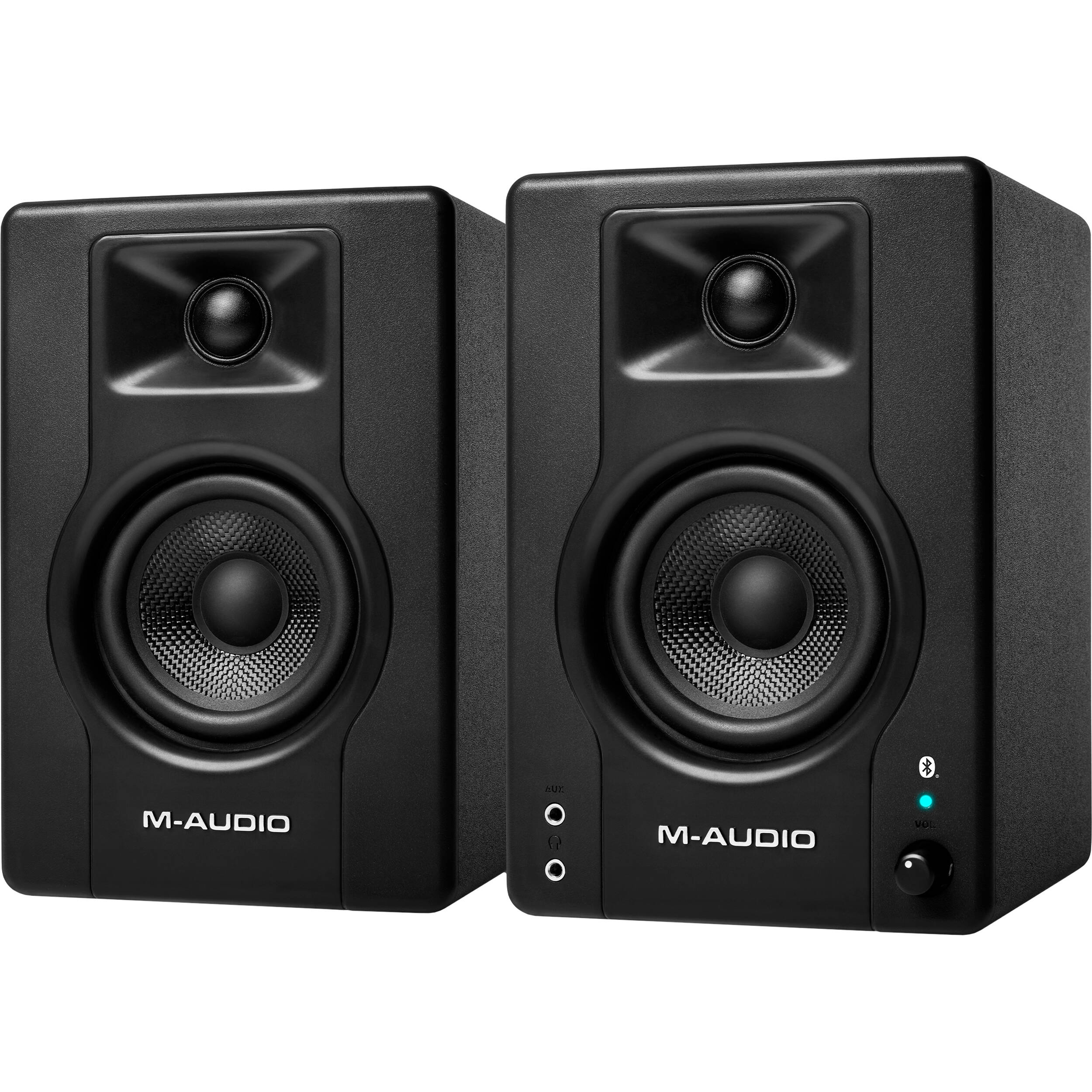 M-Audio BX3 BT desktop speakers shown on a desk with black and silver design, featuring control knobs and connection ports.