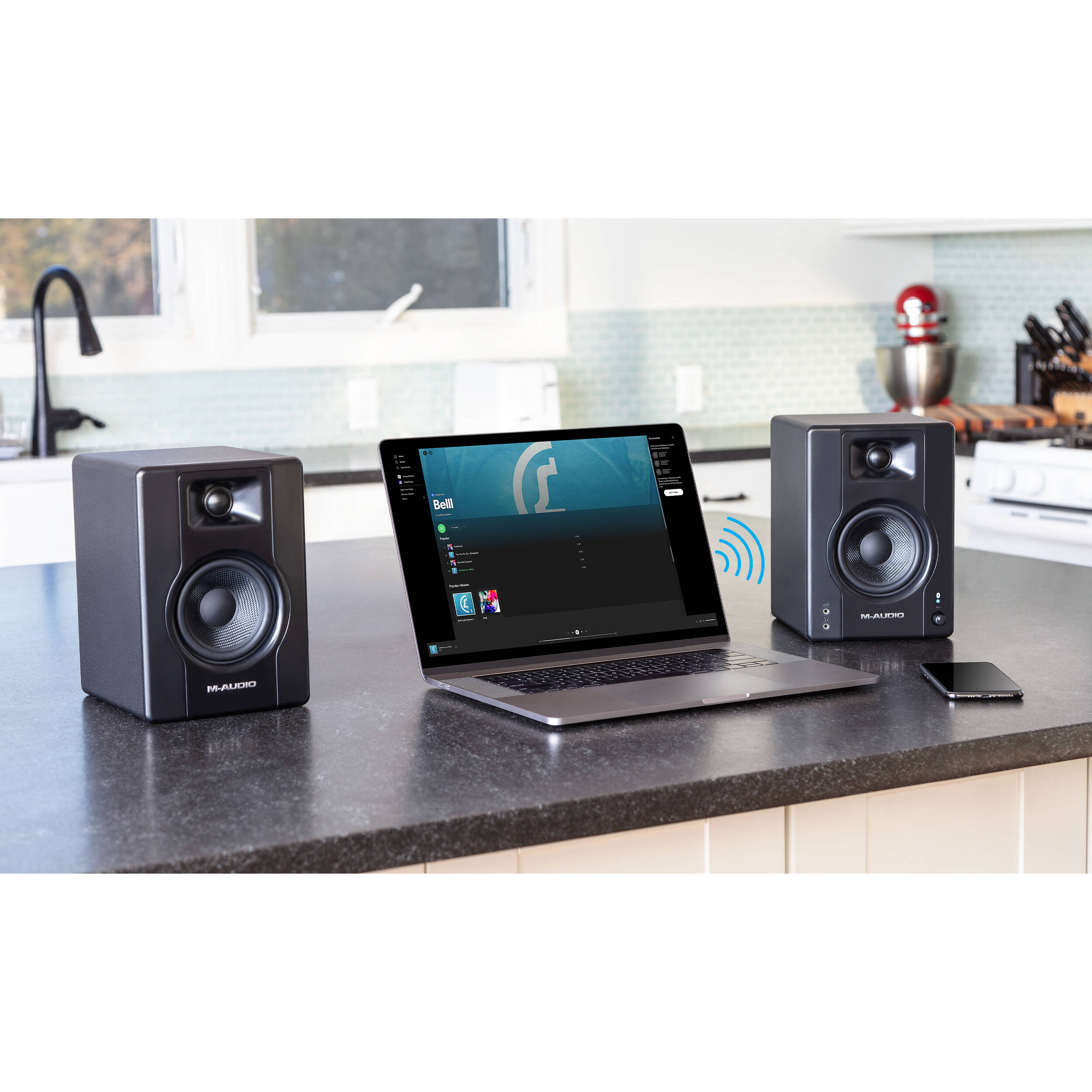 M-Audio BX3 BT desktop speakers showing black speakers with control knobs and connection ports on a desk surface.