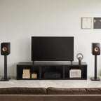 KEF LS50 Meta passive bookshelf speakers in carbon black, shown in a living room setting with sleek modern design