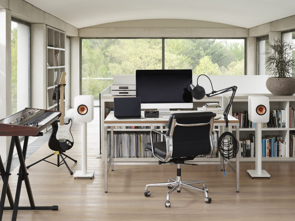 KEF LS50 Meta passive bookshelf speakers in mineral white, shown in a home studio setup with a landscape orientation.