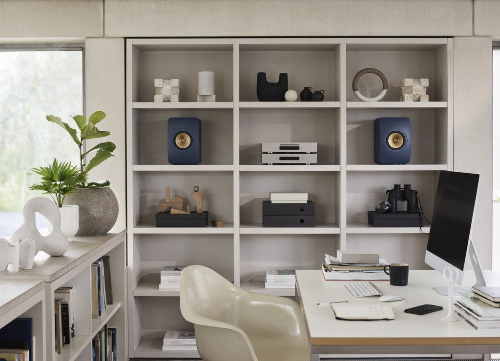 KEF LS50 Meta passive bookshelf speakers in royal blue, shown on a shelf in an office room setting.