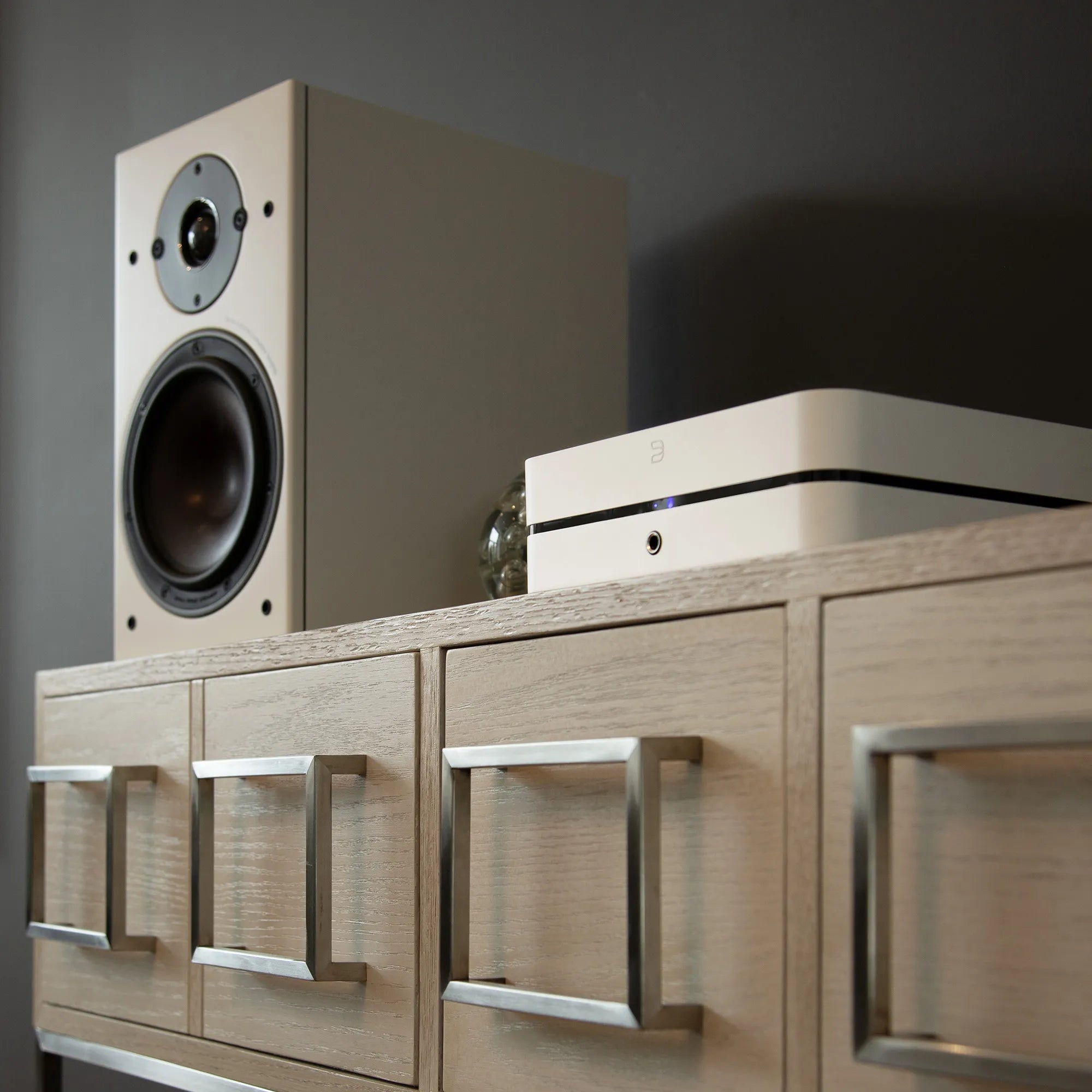 Bluesound Powernode 2025 music streamer in white, placed next to DALI Opticon 2 MK2 speakers, low right view.