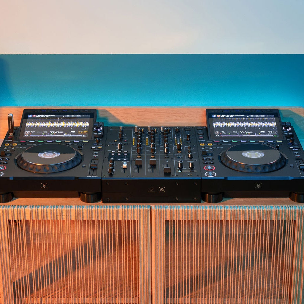 AlphaTheta DJM-V5 DJ mixer with multiple controls and input/output ports, shown in a professional music studio setting.