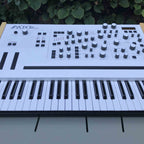 Modor NF-1k keyboard synthesizer with black casing, showing its control knobs and display screen.