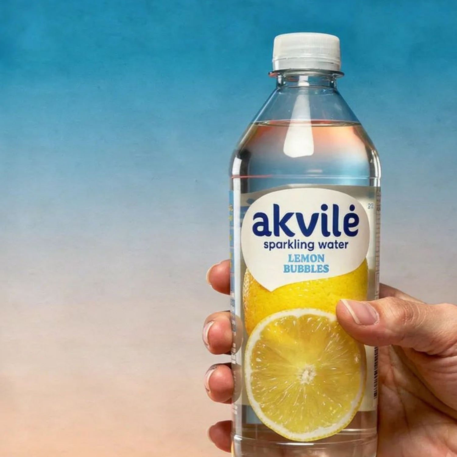 Hand holding a bottle of akvile sparkling water with lemon flavor against a blue gradient background