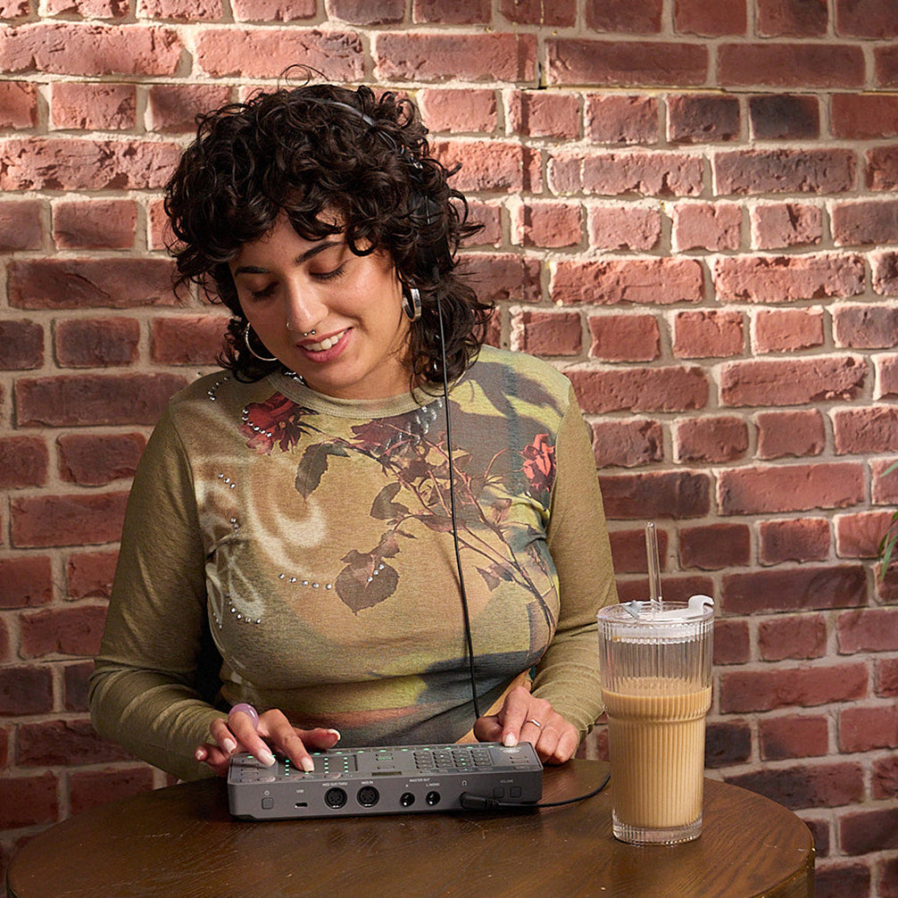 AlphaTheta ChordCat DJ pad controller, woman playing device at cafe table.