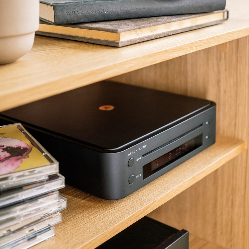Argon Audio CD1 Black on an oak shelf next to a stack of CDs