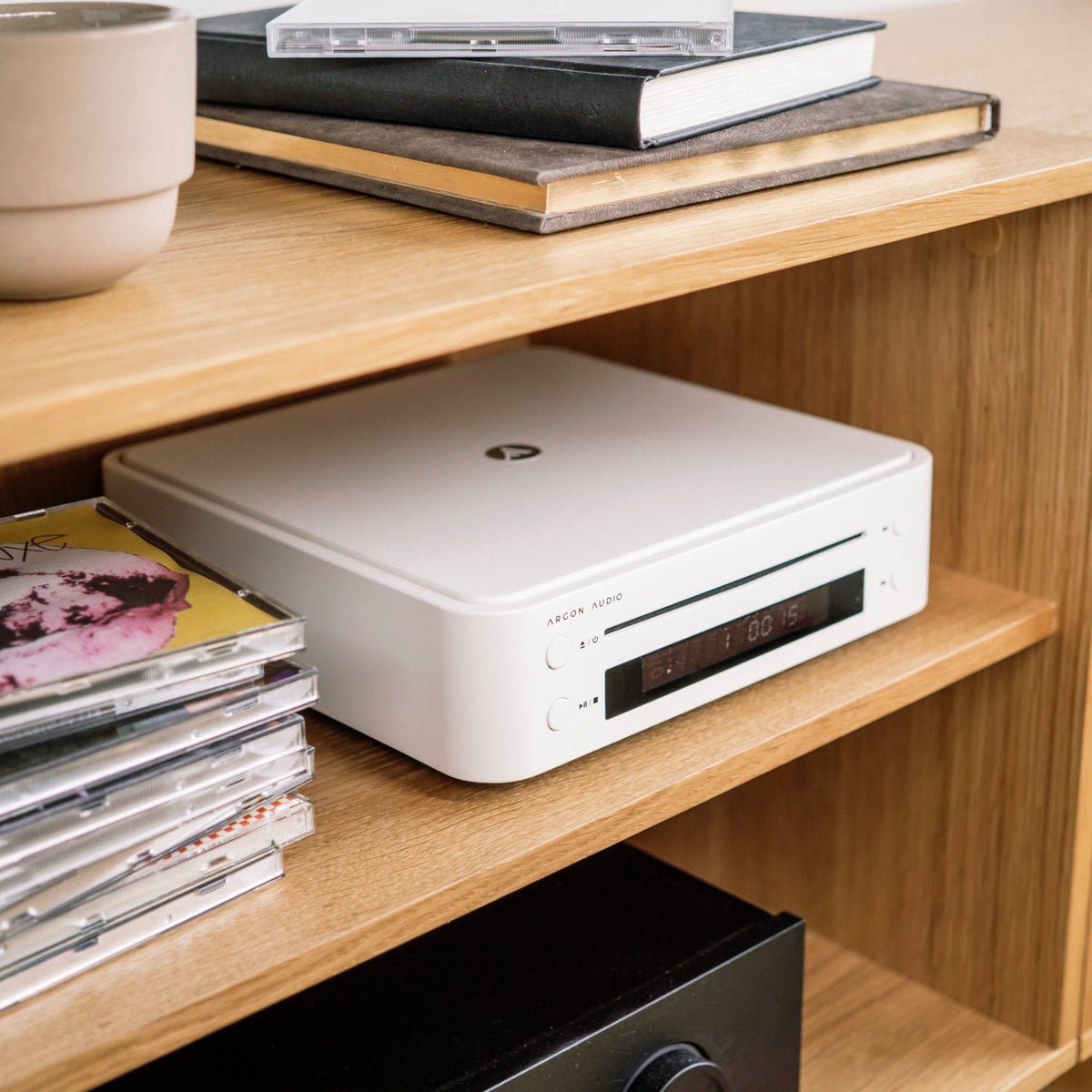 Argon Audio CD1 White on an oak shelf next to a stack of CDs