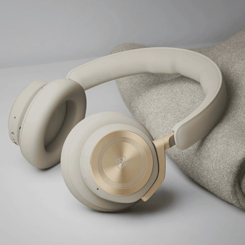 Bang & Olufsen Beoplay HX wireless headphones in gold-tone, shown in a lifestyle setting with sleek design and comfortable fit