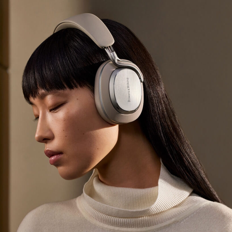 Bowers & Wilkins Px8 S2 wireless headphones in warm stone color worn by a woman, featuring sleek design and premium audio features.