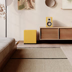 Dali Basik Sub in Golden Yellow placed beside an oak sideboard in a minimal interior