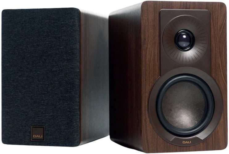 DALI Kupid passive bookshelf speakers shown in a modern living room setting, highlighting their sleek black design and compact size.