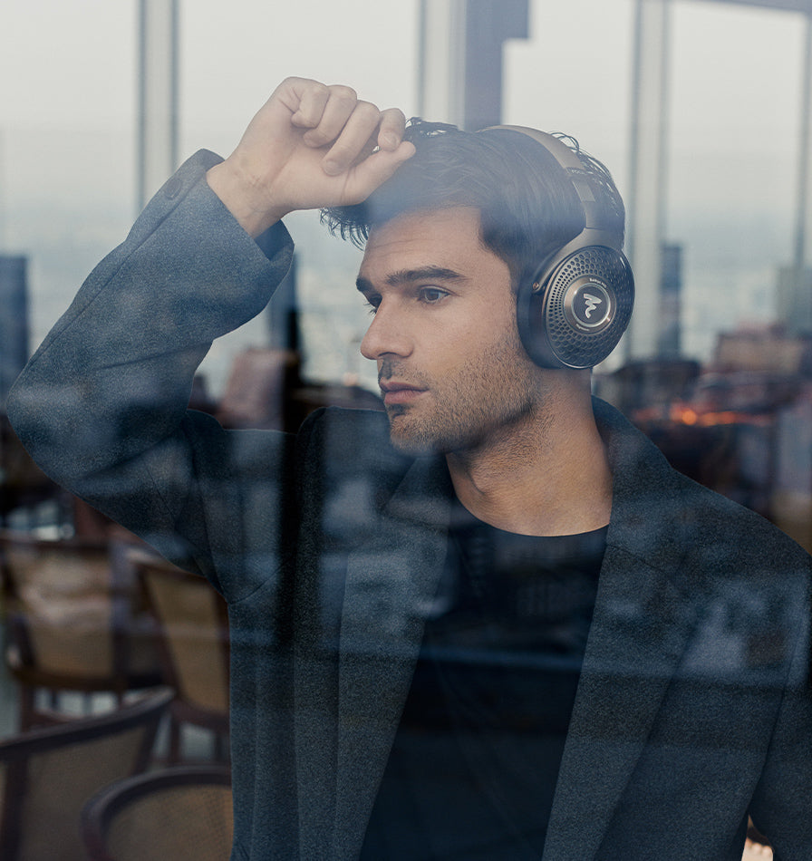 Focal Bathys MG wireless headphones worn by a man, viewed from behind through a glass window, showcasing sleek black design.