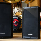 Mackie Thrash15v2 and Thrash12v2 powered PA speakers set up in a rehearsal room next to a drum kit