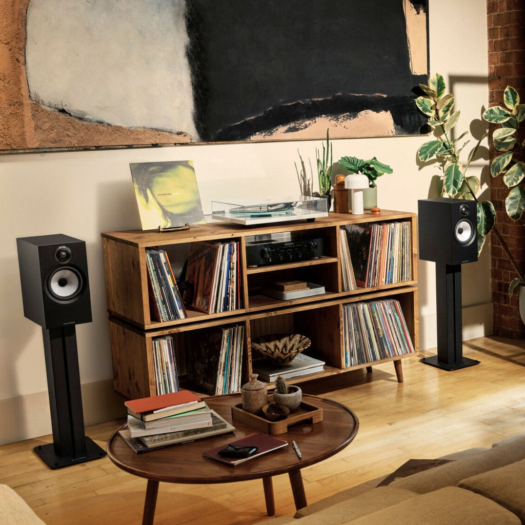 Bowers & Wilkins 606 S3 passive bookshelf speakers in black, shown with matching FS-600 S3 speaker stand on a modern living room setup.