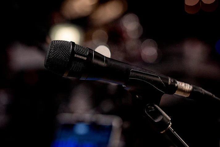 Shure Nexadyne 8/C dynamic microphone shown in a professional environment with a sleek black design and microphone grille.