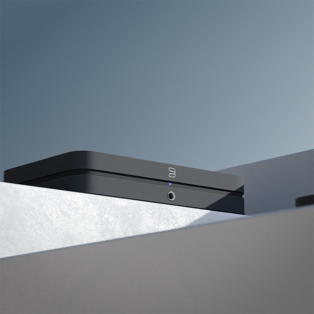 Bluesound Node 2025 black music streamer with sleek design and front display, connected to audio equipment.