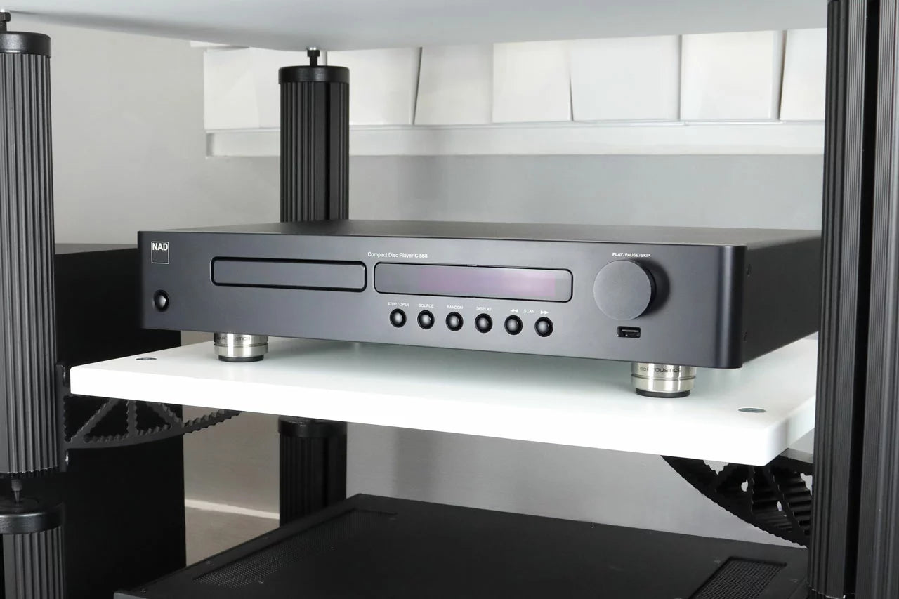 IsoAcoustics Orea Graphite speaker stands shown in a modern living room setting, designed to elevate and stabilize speakers.