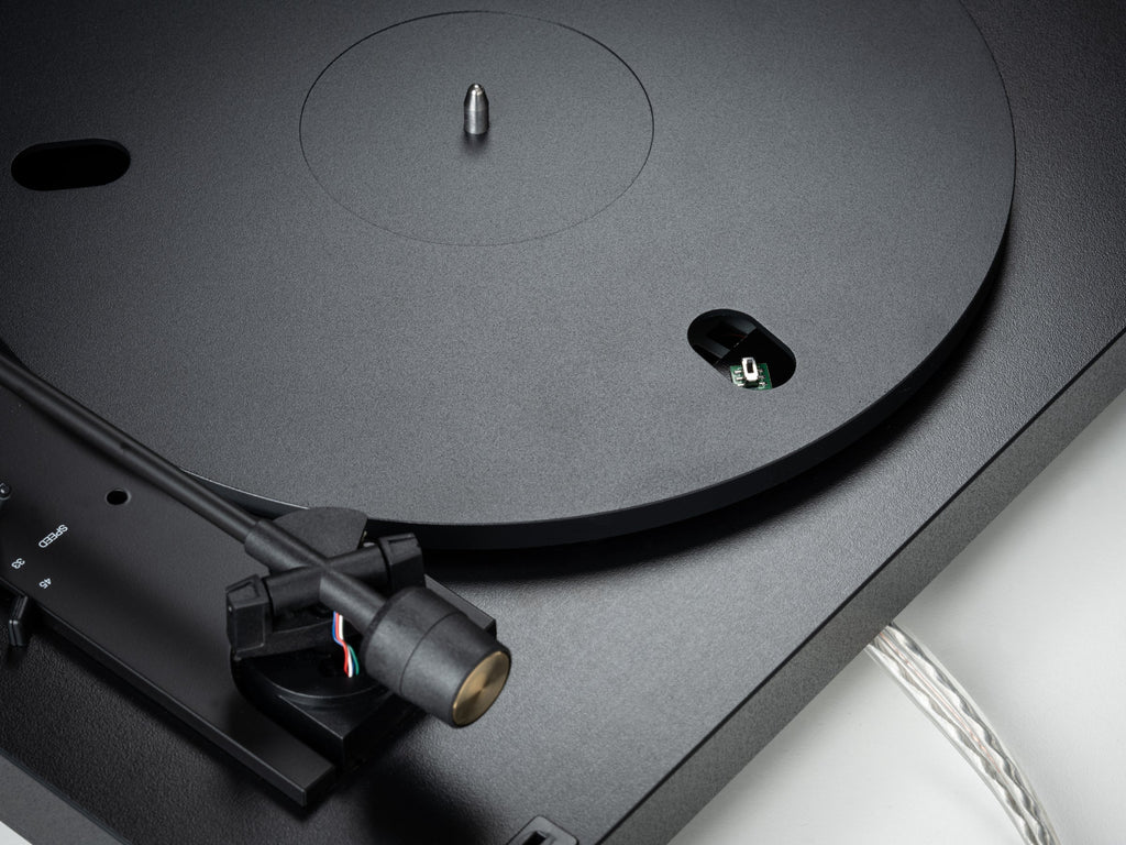 Pro-Ject Automat A1.2 turntable with sleek design, featuring a wooden plinth, tonearm, and platter, set in a stylish living room.