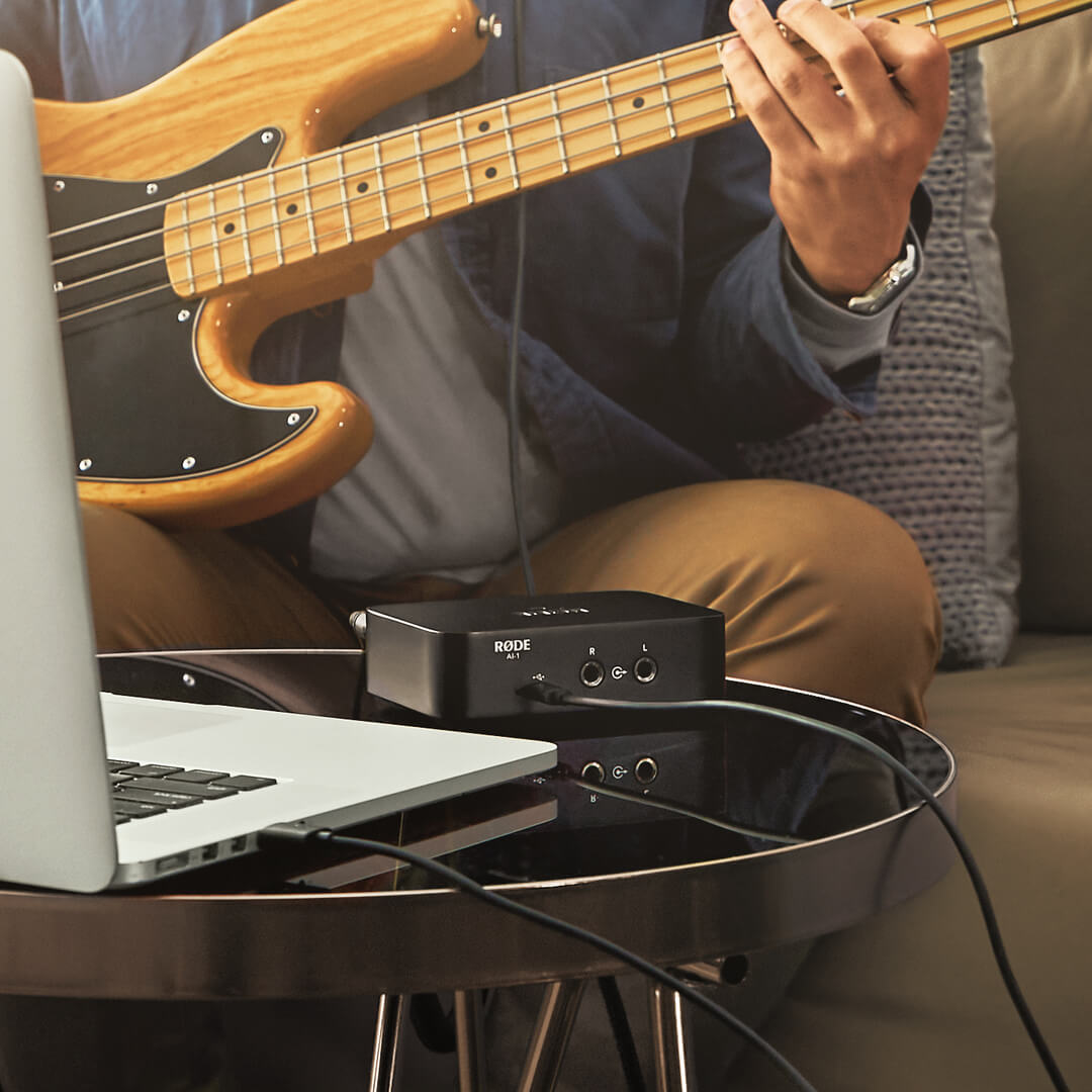 Rode AI-1 audio interface kit with guitar and musician seated on a couch, demonstrating professional recording setup.