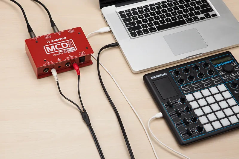 Samson MCD2 Pro DI box connected to a laptop, showing professional audio equipment for live sound and recording setups.