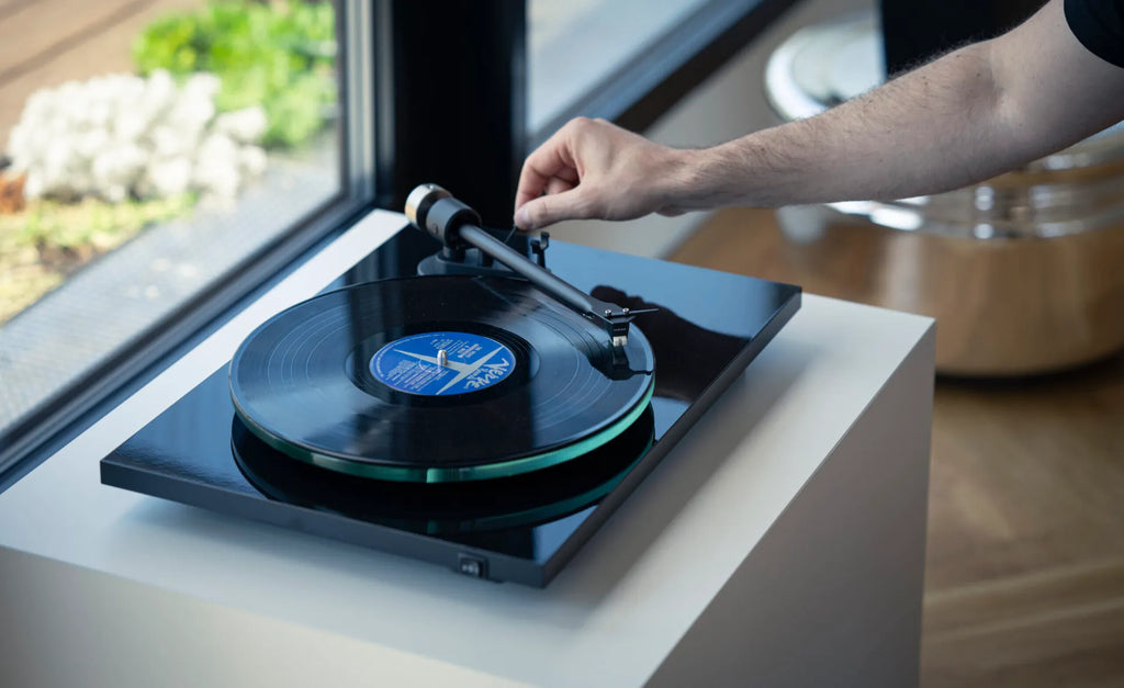 Pro-Ject T2 W turntable with wooden plinth and tonearm, shown in a modern living room setting.
